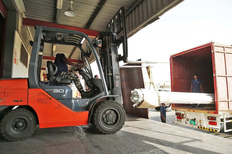 Small crane loading pipes into a truck for land transport at Al Talib shipping service storage facility